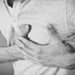 Sintomas de infarto feminino e masculino: mulher segurando o peito com dor no peito