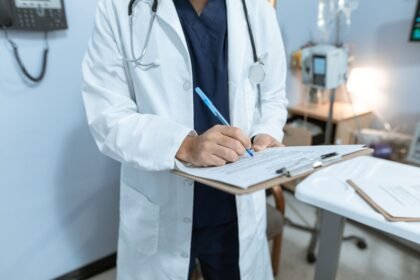 Médico de jaleco preenchendo atestado médico em prancheta, representando a emissão de um atestado médico rápido