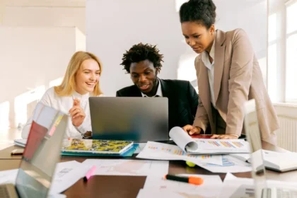 Três profissionais reunidos analisam materiais e informações em um notebook